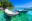 Two wooden boats moored in crystal clear jade green water with wooded island beyond