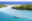 A white sailing boat sits in a tranquil bay of turquoise water. Two small headlands covered in lush vegetation overlook a narrow channel and two fond-covered gazebos sit just offshore