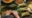 Close up of man's hands rolling a palm fond around food with finished parcels tied with raffia and bowls of meat sitting off to one side