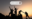 Hikers at sunrise atop rocks, their hands in the air with one helping another to scramble over a rock