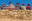 Five women sitting on top of a stone wall wearing colourful shawls and round, wide-brimmed felt hats alongside a child in a baseball cap and orange jacket.