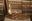 Glasses of wine and an open bottle sitting on a wine barrel in a cellar with bottles on shelves behind